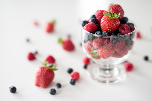 Glass cup of raspberries and cup of starberries on white table.