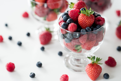 Glass cup of raspberries and cup of starberries on white table.