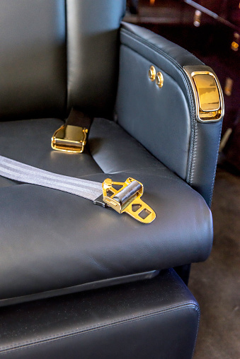 Close-up of luxury golden seat belt and part of leather seat of private jet. Traveling in comfort by upper class.