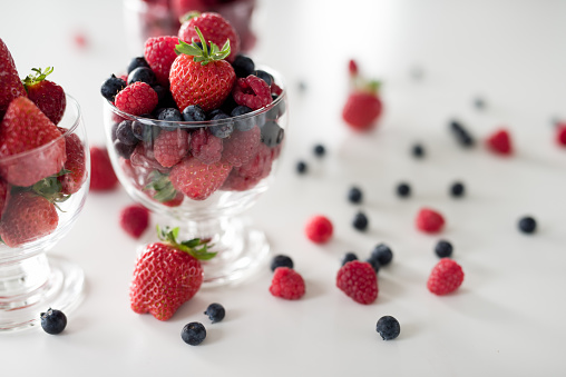 Glass cup of raspberries and cup of starberries on white table.