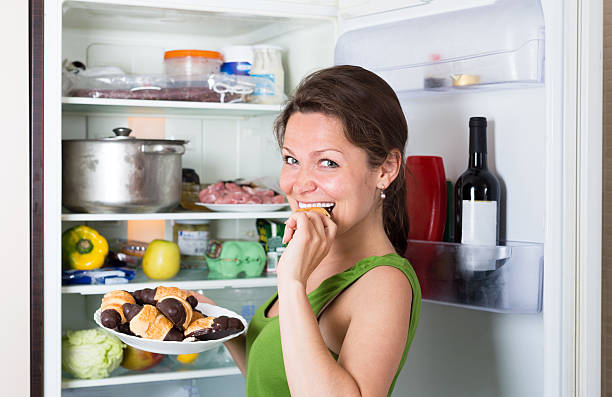istock Woman opening refrigerator and eating cakes 495988696