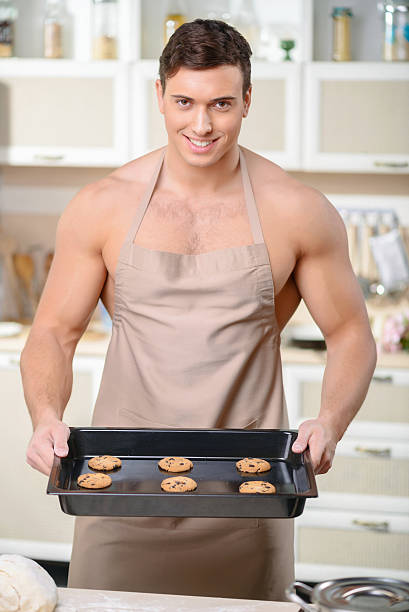Perfect cookies. Young athletically built cook is demonstrating a tray of fresh homemade chocolate chip cookies.