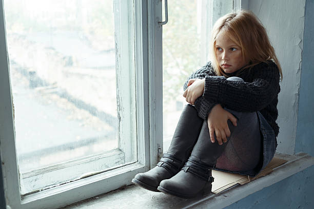 istock Depressed poot girl standing near window 496025808