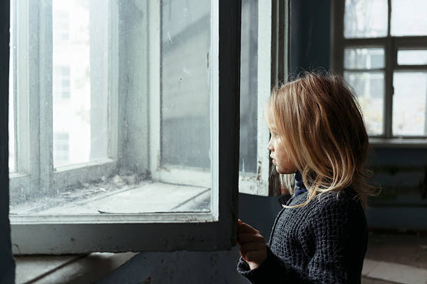 istock Depressed poot girl standing near window 496025862