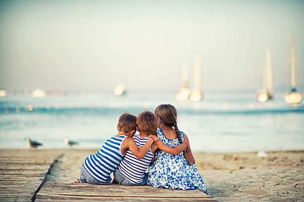 niños de descanso en la playa en el atardecer y abrazar - three boys fotografías e imágenes de stock