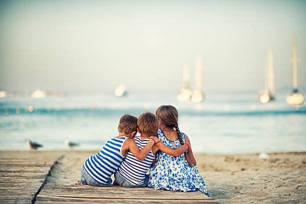 bambini seduti sulla spiaggia di sera e accoglienza - three boys foto e immagini stock