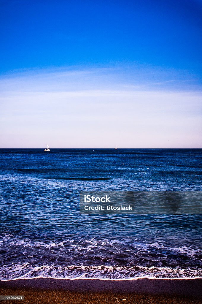 Spanish Beach with sailboat in the distance. Waves crashing on a beach in Spain. Barcelona - Spain Stock Photo