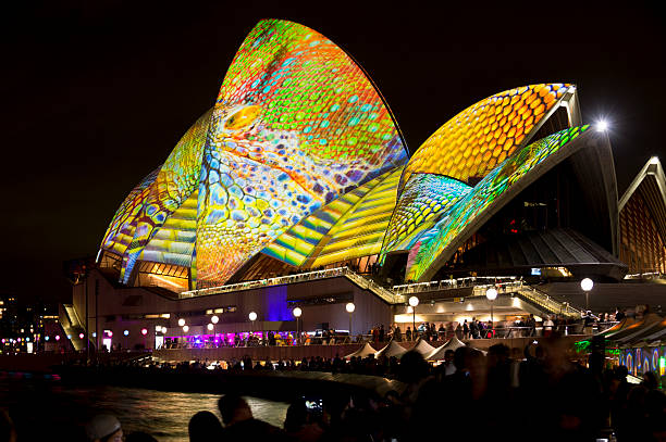 Sydney, Australia - May 29, 2014: Animated images and colourful designs projected onto the sails of the Sydney Opera House for the Vivid Sydney festival at Sydney Harbour. Crowded Opera Bar in the foreground.