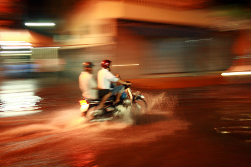 This photo shows two Vietnamese men riding a motorbike on a flooded street at night during the monsoon season. Ho Chi Minh City, Vietnam; Blurred motion through panning technique