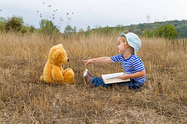 ragazza carina lettura libro orsetto - outdoors looking at camera little girls child foto e immagini stock