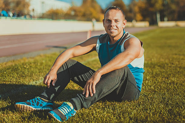 istock Sporting man sitting on grass and rests in the stadium. 496072062