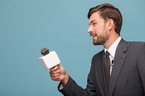 Attractive young reporter is interviewing someone. He is standing in profile and holding a microphone. The man in suit is smiling. Isolated and copy space in left side