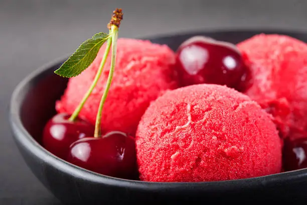 Photo of Cherry, raspberry, strawberry, cranberry , red sorbet,scoop, black stone background.