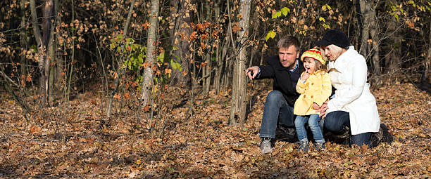 European Family Father Mother and Little Baby Girl sitting in Autumnal Forest Pointing on something Watching and Looking