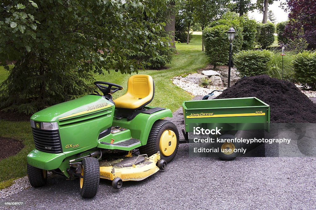 John Deere with Wagon New Cumberland, PA, USA - June 14, 2011 : John Deere tractor with wagon in front of pile of garden mulch in a residential back yard Lawn Mower Stock Photo