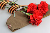 Military cap, carnations tied with Saint George ribbon on gray
