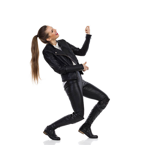 Rock Girl Plays The Air Guitar Young woman in black leather trousers, jacket and boots playing the air guitar and looking away. Side view. Full length studio shot isolated on white. air guitar stock pictures, royalty-free photos & images