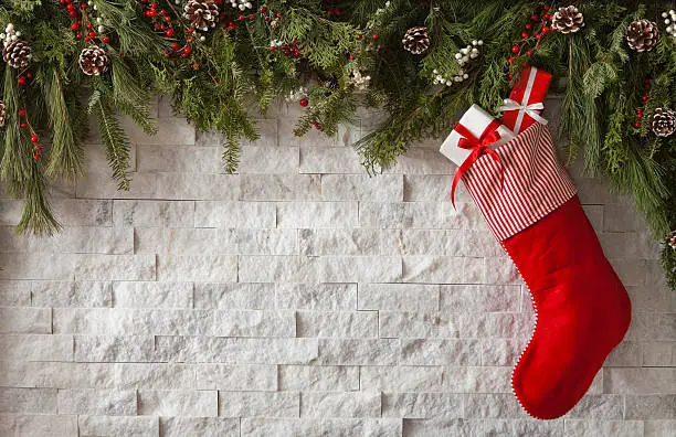Christmas Stockings with gifts and bows hung on a fireplace with evergreen garland. Copy space.
