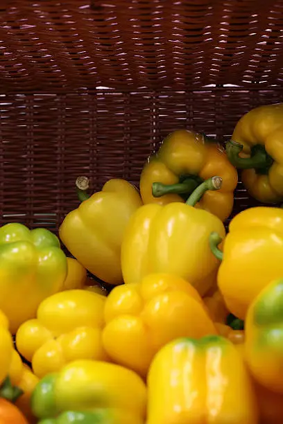Closeup seasoning fresh vitamin yellow colored bell sweet spicy flavoring peppers in half empty semi-vacant flat-bottom basket, vertical picture