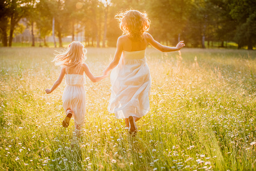 Mother and little daughter running across a golden meadow.