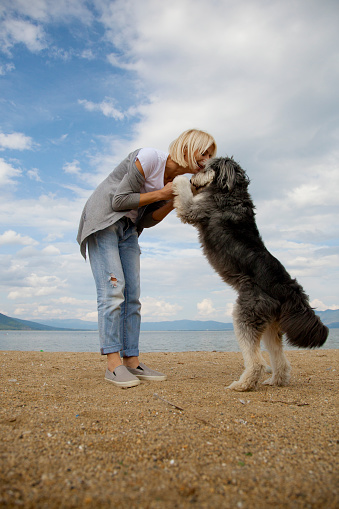 young beautiful woman kissing her dog, standing outdoor at beach