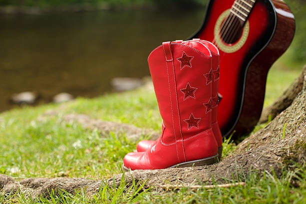 cowgirl boots standing on tree with a red guitar close to the river