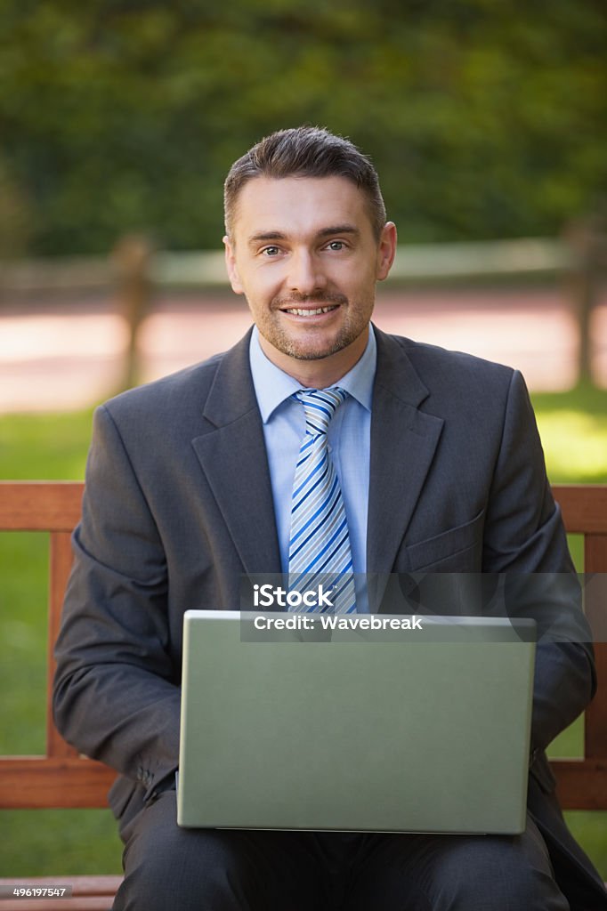 Businessman using laptop on bench in park Portrait of a smart young businessman using laptop on bench in the park 30-39 Years Stock Photo