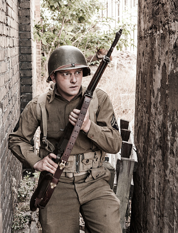 Re-enactors Armed Rifles And Dressed As World War Ii German Wehrmacht Infantry Soldiers Fighting Defensively In Trench. Fight Against Combat Vehicle. Building On Fire On Background. Black White Colors.