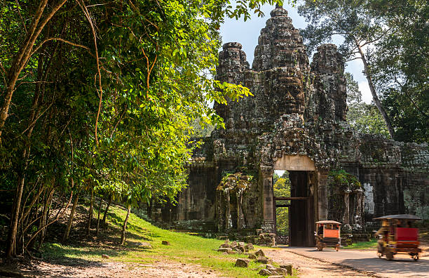 Magnificent ancient gate leading to Angkor Thom in Cambodia. Angkor Thom temple belongs to the Angkor Wat Heritage site; on the picture two tuk yuk vehicles drive tourist passengers.