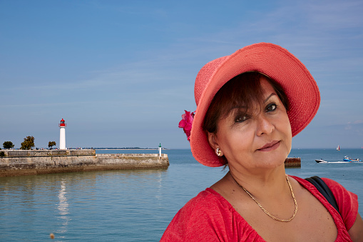 Mature smiling hispanic woman in sunhat at the coast