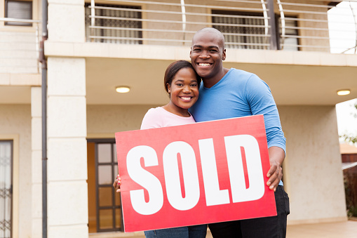 portrait of young couple holding sold sign outside their house