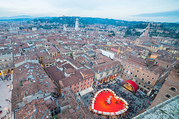 Verona, Italy - February 14, 2014: People walk in the Piazza Dante (Courtyard of the old market), where a large red heart has been placed. For the Valentine's day Verona is transformed into the city of love, with ornaments and lights in the squares and alleys of the historical center, and the stalls of Piazza dei Signori offer local products.