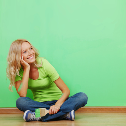 Female house painter sitting with paintbrush near wall