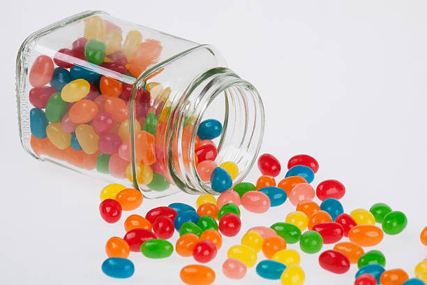 istock Jelly Beans spilled from glass jar isolated on white background 496241848