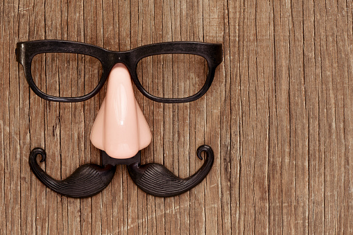 a fake mustache, nose and eyeglasses on a rustic wooden surface