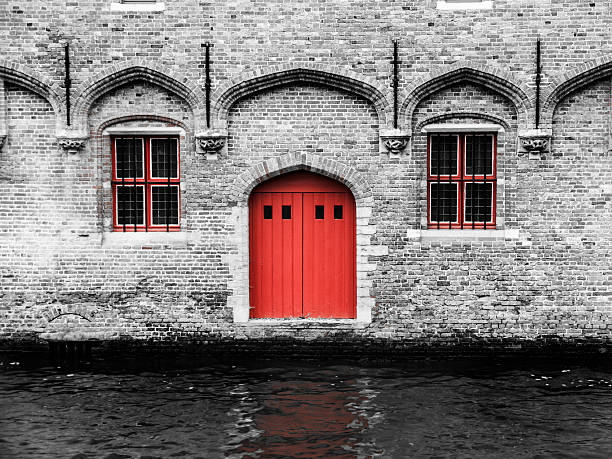 Red door and two windows at water canal. Typical architecture of Bruges, Belgium.