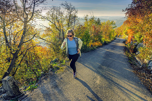 Caucasian mature woman running at sunset in autumn, Slovenia, Europe Mature  woman running on the asphalt road at sunset, smoke bush,lens flare, Sabotin, Nova Gorica,Primorska, Slovenia, Europe.  Autumnal coloures.Nikon D3x primorska white sport nature stock pictures, royalty-free photos & images