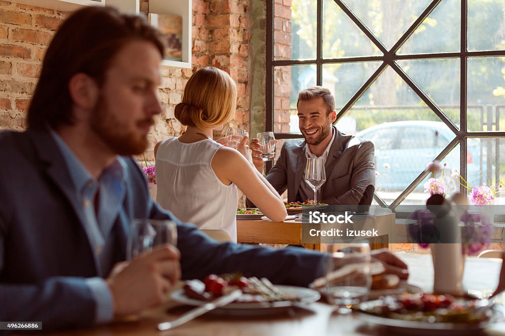 Business colleagues enjoying lunch in the restaurant Business colleagues enjoying lunch in the restaurant. Focus on background. On the foreground bearded man eating steak.  Business Stock Photo