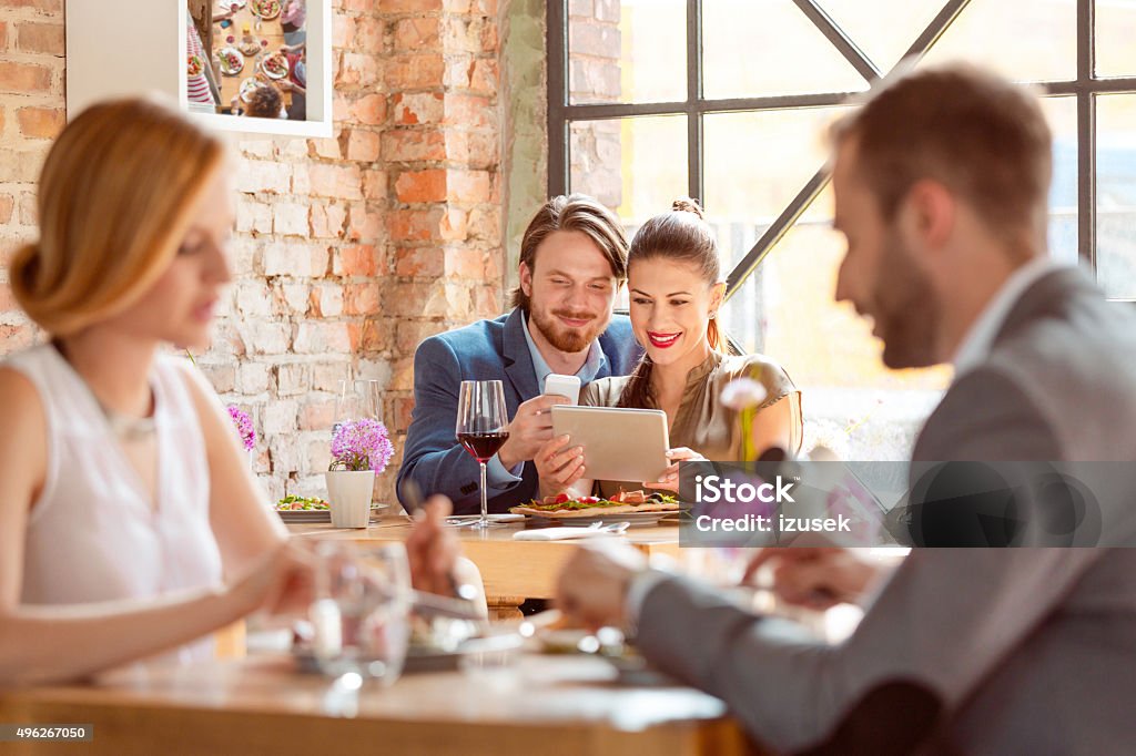 Elegant couple using a digital tablet in the restaurant Happy couple using a digital tablet together during lunch in the restaurant, eating pizza and drinking red wine. 2015 Stock Photo