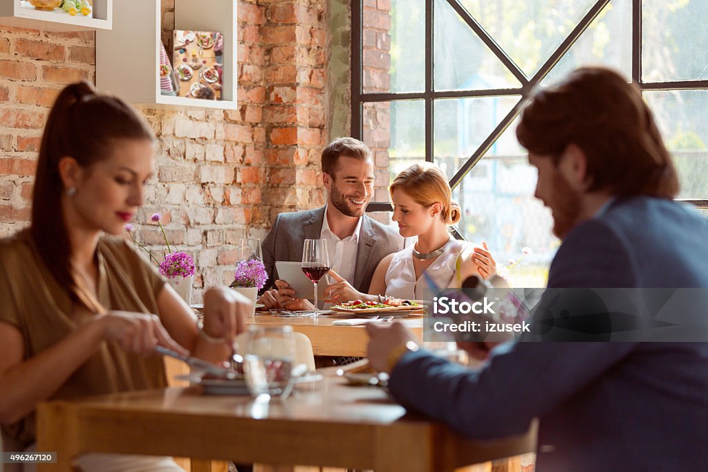 Elegant couple using a digital tablet in the restaurant Two couples enjoying meal in the restaurant. Focus on happy couple using a digital tablet, eating pizza and drinking red wine. 2015 Stock Photo