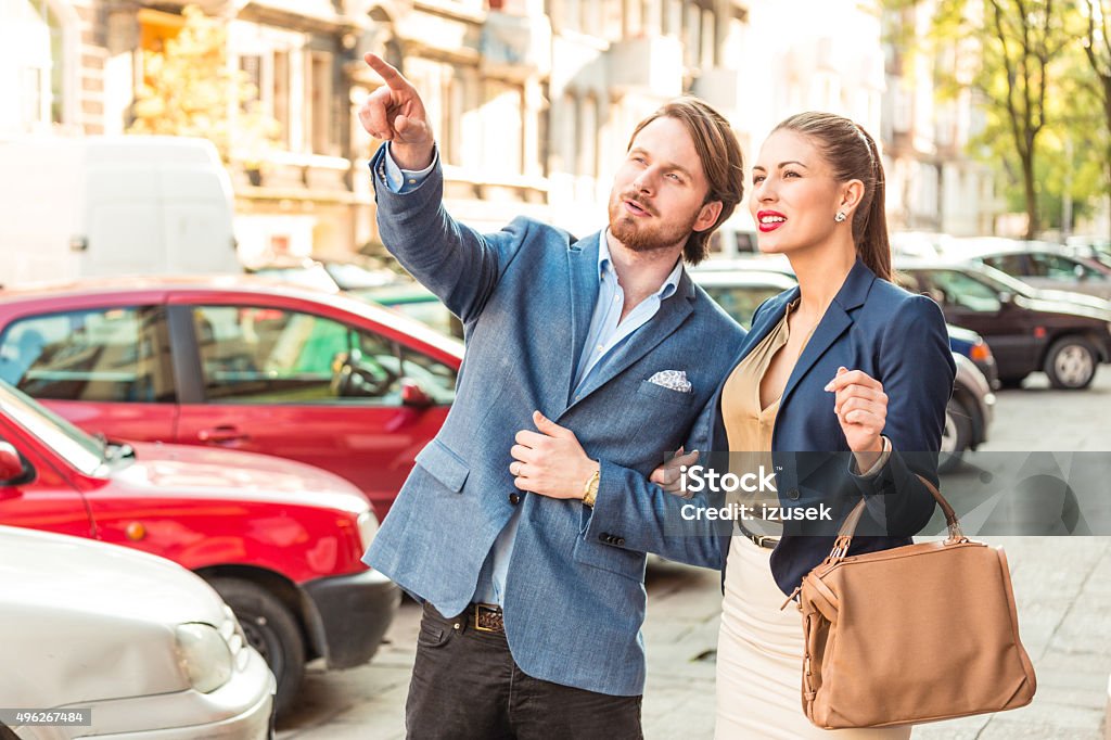 Elegant couple in the european city, man pointing with finger Happy elegent couple standing on the sidewalk in the european city, man pointing with index finger. Business Stock Photo