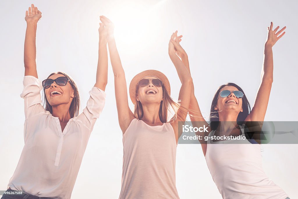 Enjoying life. Low angle view of three beautiful young women holding hands and raising their arms up Three People Stock Photo