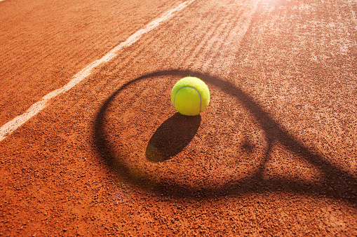 Tennis ball and racket shadow on clay court.