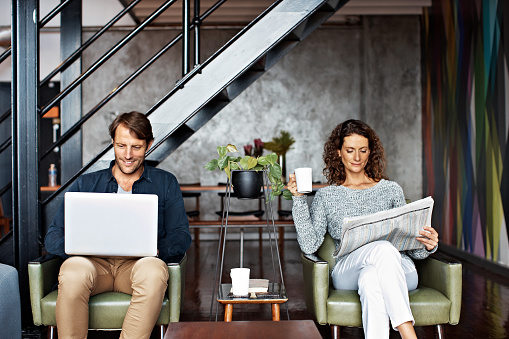 Shot of a content mature couple sitting in their living room reading the newspaper and using a laptop