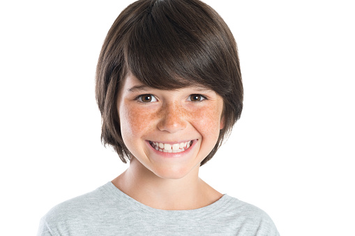 Closeup shot of little boy smiling with freckles. Portrait of happy male child looking at camera isolated on white background. Happy cute boy with brown hair standing against white background.