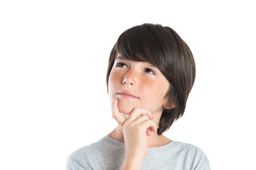 Portrait of cute boy thinking isolated on white background. Closeup shot of boy thinking with hand on chin. Male child with freckles looking up and contemplates isolated on white background.