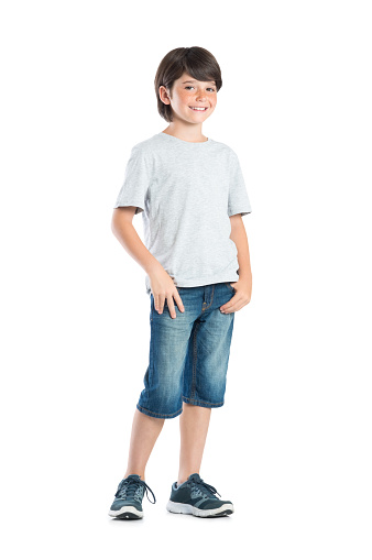 Handsome male kid with long, fair hair, dressed in sand-colored shirt and black pants. Posing in front of a white studio background and looking at the camera. Full length image.