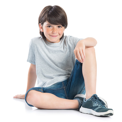 Closeup shot of smiling little boy sitting on white background. Adorable child in casual looking at camera. Happy cute boy sitting on floor and looking at camera.