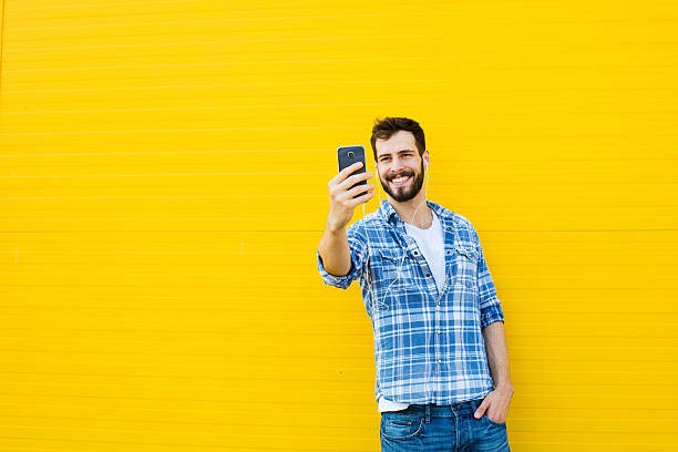 young handsome man with headphones on yellow wall stock photo