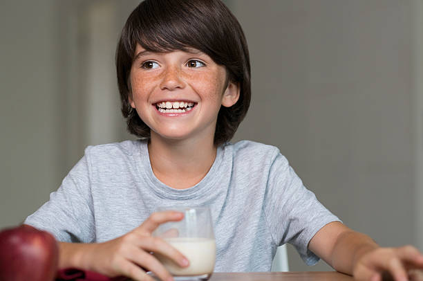 Boy having healthy breakfast Portrait of smiling boy drinking glass of milk. Child laughing during healthy breakfast at home before going to school. Happy smiling boy drinking milk and eatin a red apple. food elementary student healthy eating schoolboy stock pictures, royalty-free photos & images